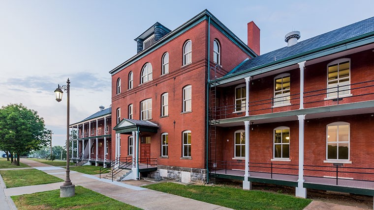 A three-story red brick barracks building with white porches at Jefferson Barracks, photographed at dusk