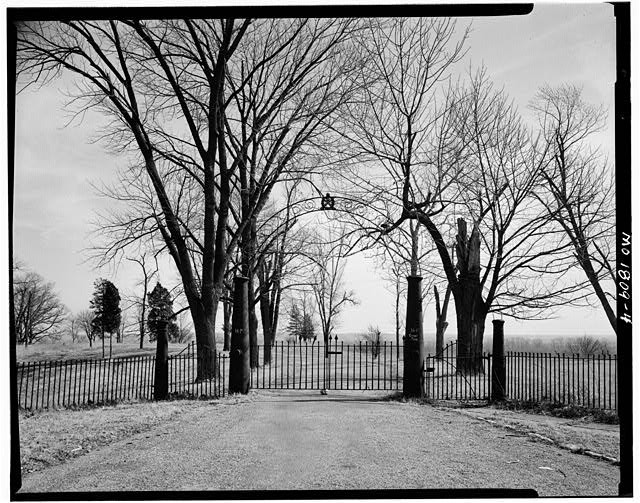 An iron entrance gate at Jefferson Barracks, flanked by stone gateposts and bare trees, in a black and white archival photograph