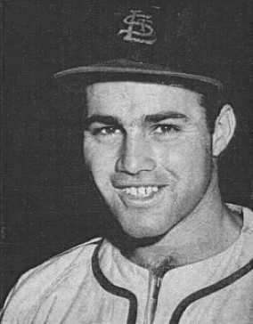 Black and white portrait of a smiling young Joe Garagiola in a St. Louis Cardinals cap and uniform