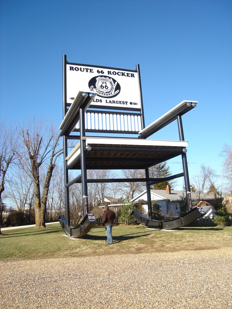 An enormous steel rocking chair, several stories tall, with a person standing beneath it for scale and a Route 66 Rocker sign on the back