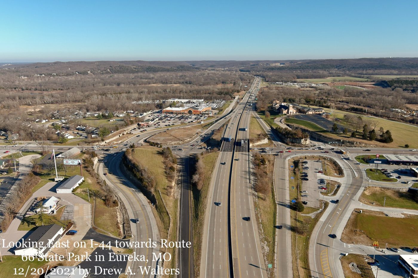 Aerial view of a multi-lane interstate highway and its interchange ramps cutting through winter hills, with the river valley in the distance