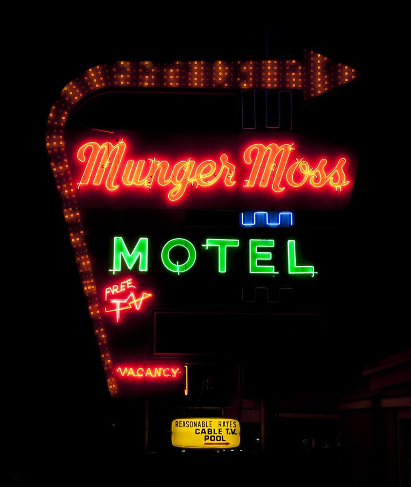 A tall red neon motel sign reading Munger Moss Motel with a yellow arrow of chasing bulbs, lit up against a black night sky