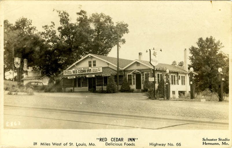 A sepia real-photo postcard of a low log building with a shingled roof and a sign, captioned Red Cedar Inn, 28 Miles West of St. Louis, Mo., Delicious Foods, Highway No. 66