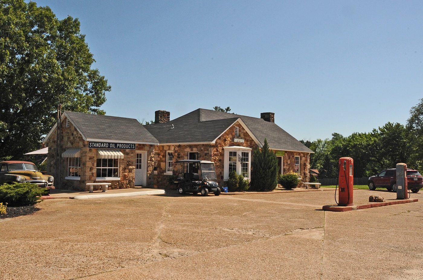 A small stone building with a steep gabled roof and a red gas pump out front on a gravel lot