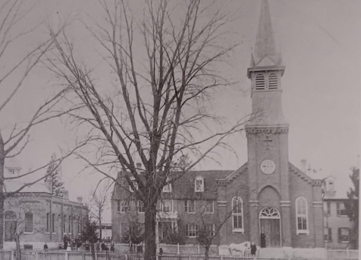 Sepia photograph of a brick church with a square bell tower beside a two-story convent building, bare trees in front