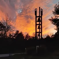 The three-bell tower silhouetted against a fiery sunset sky