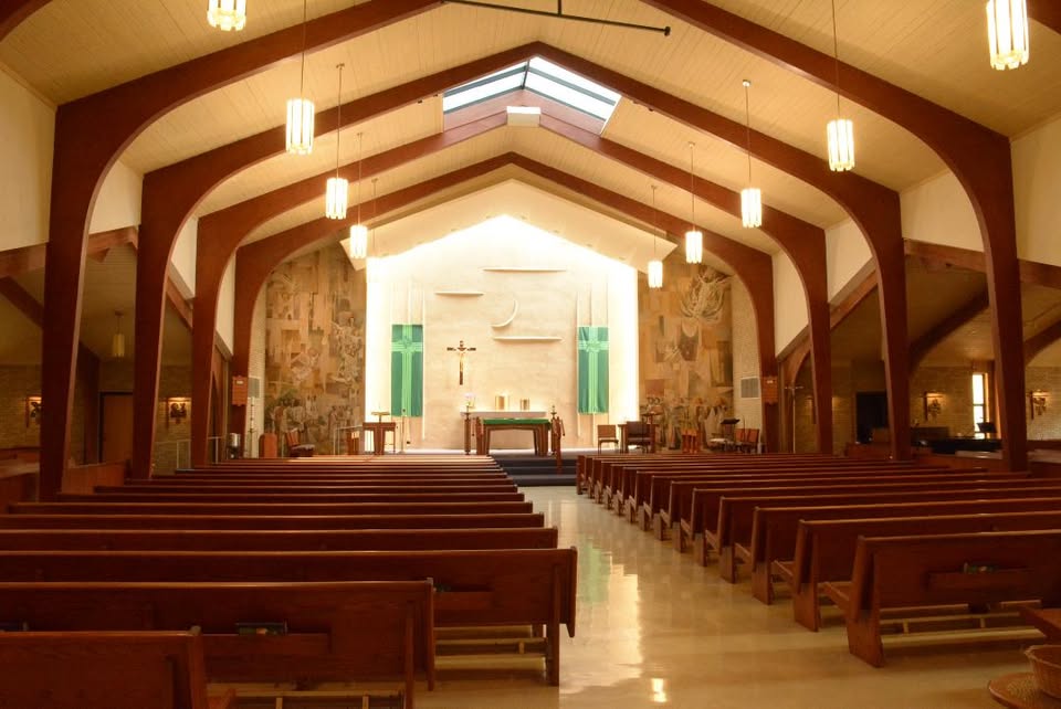 The sunlit interior of Our Lady Queen of Peace, with wooden arches and pews leading to the altar